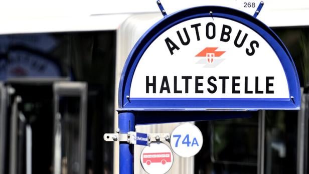 Ein blaues Haltestellenschild für den Autobus 74A steht vor einem roten Bus, eine Person steigt ein.