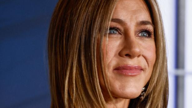 Jennifer Aniston mit langen Haaren und schwarzem Kleid blickt nach rechts.