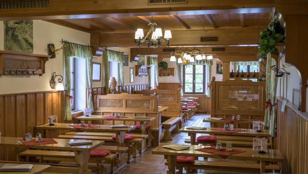 Gemütlicher Gastraum mit Holzmöbeln, roten Sitzpolstern und dekorativen Lampen.