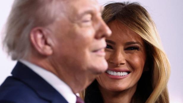 Donald Trump steht im Profil, während Melania Trump lächelt.