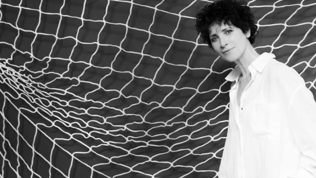 Eine Frau mit lockigem Haar und weißem Hemd steht vor einem Netz.