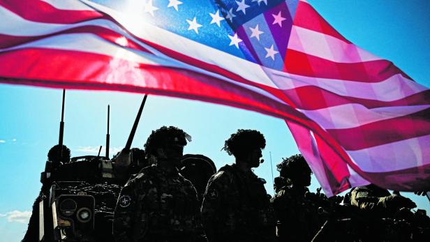 Soldaten stehen vor einem Panzer unter einer wehenden US-Flagge.