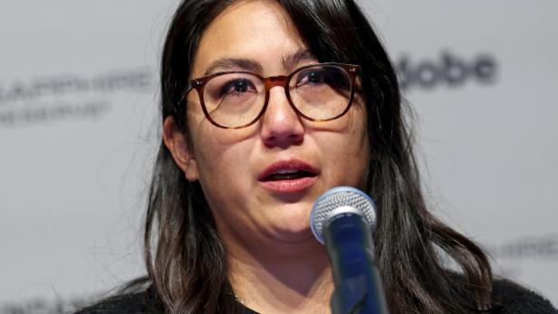 Eine Frau mit Brille und langen dunklen Haaren spricht emotional in ein Mikrofon.