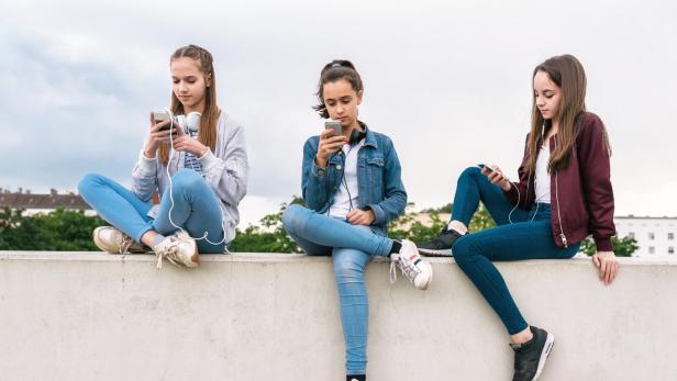 three teenage girls with smartphones sitting on wall