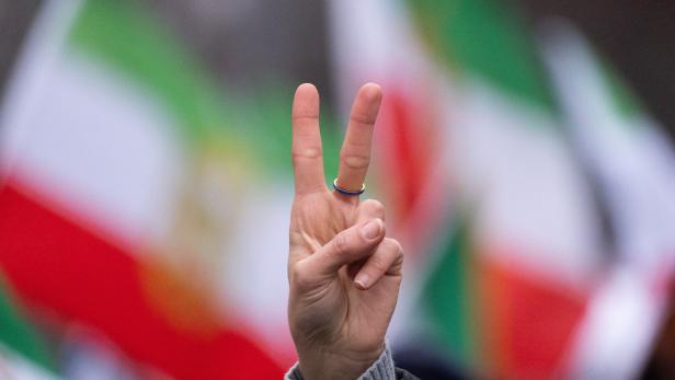 Eine Hand zeigt das Victory-Zeichen vor unscharfen Flaggen in Grün, Weiß und Rot.