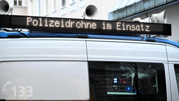 Ein Polizeifahrzeug mit Lautsprechern zeigt auf einer Leuchttafel die Warnung „Polizeidrohne im Einsatz“.