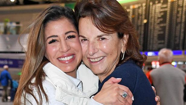 Claudia Obert und Eva Benetatou umarmen sich am Flughafen und lächeln in die Kamera.