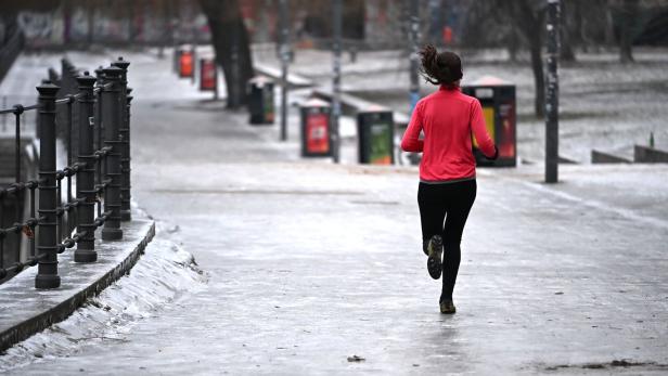 Eine Person joggt auf einem vereisten Gehweg entlang eines Geländers in einer winterlichen Umgebung.
