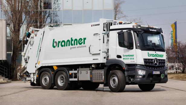 Weißer Müllwagen der Marke Brantner vor einem Gebäude.