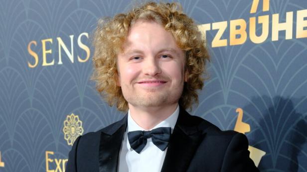 Ein Mann im Smoking hält einen gelben Pfannenwender in der Hand.