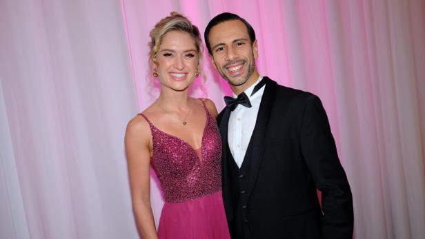 Eine Frau im glitzernden pinken Abendkleid steht lächelnd neben einem Mann im schwarzen Smoking mit Fliege.