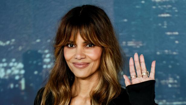 Halle Berry in schwarzem Kleid mit tiefem Ausschnitt und glitzerndem Rock winkt.