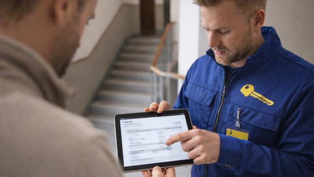 Schlüsseldienst-Mitarbeiter erklärt einem Kunden eine Rechnung auf einem Tablet im Stiegenhaus.