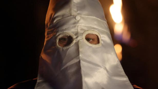 Eine Person mit einer weißen Kapuze und Augenausschnitten blickt in die Kamera.