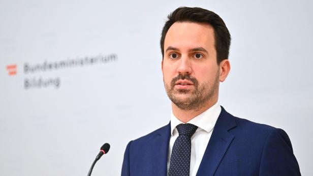 Ein Mann im Anzug spricht an einem Mikrofon vor einer Wand mit der Aufschrift „Bundesministerium Bildung“.