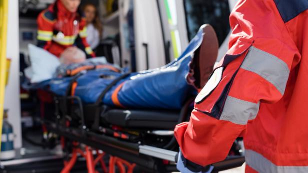 Selective focus of paramedic in uniform carrying stretcher with patient in ambulance ca outdoors