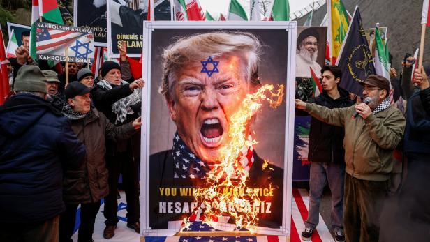 Männer verbrennen ein Plakat, wo US-Präsident Trump abgebildet ist