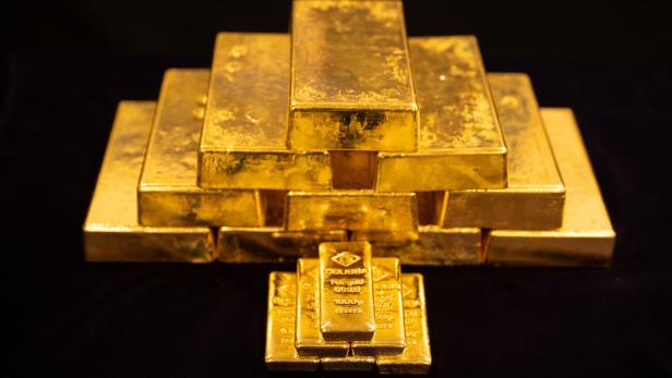 Mehrere goldene Barren sind pyramidenförmig aufeinander gestapelt und liegen auf dunklem Untergrund.