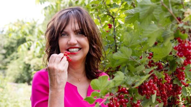 Eine Frau im pinkfarbenen Kleid isst rote Johannisbeeren vom Strauch.