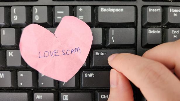 Love Scam awareness concept. A person typing on keyboard sending message to scammer and a crumpled heart with the text Love Scam written on placed on the keyboard
