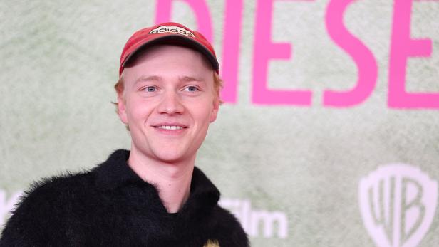 Bruno Alexander lächelt bei einer Filmpremiere vor einem Hintergrund mit Warner Bros.-Logo und großem Schriftzug.