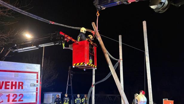 Feuerwehrleute arbeiten nachts mit einem Kran an einer beschädigten Stromleitung und sichern den Bereich.