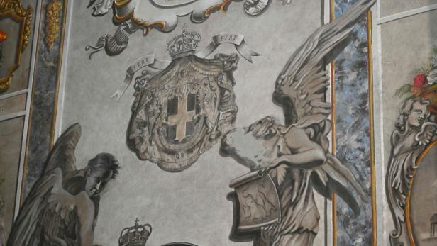 Zwei gemalte Engel halten ein Wappen mit Kreuz und Krone sowie eine Tafel mit Löwen, umgeben von barocken Verzierungen.