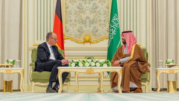 Zwei Männer sitzen sich in einem prunkvollen Raum gegenüber, hinter ihnen stehen die Flaggen Deutschlands und Saudi-Arabiens.