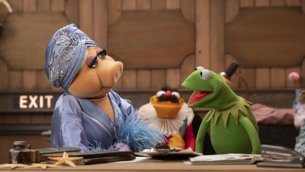 Miss Piggy und Kermit der Frosch sitzen an einem Schreibtisch, im Hintergrund ist ein weiterer Muppet zu sehen.