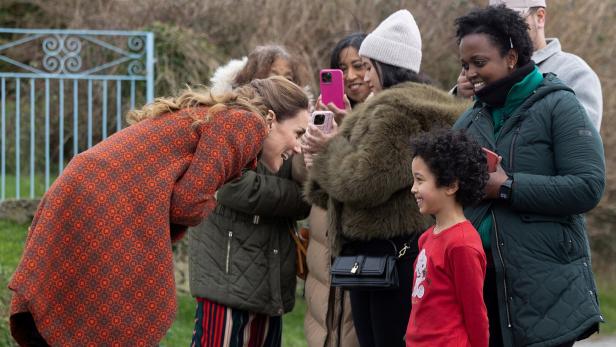 Kate beugt sich lächelnd einem Kind zu, während Umstehende Fotos machen.