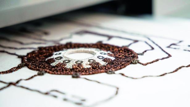 Nahaufnahme einer gestickten Leiterbahn mit kupferfarbenem Garn auf weißem Stoff.