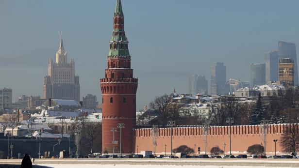 Im Vordergrund steht ein Turm des Moskauer Kremls mit rotem Stern, dahinter die Skyline der Stadt im Winter.