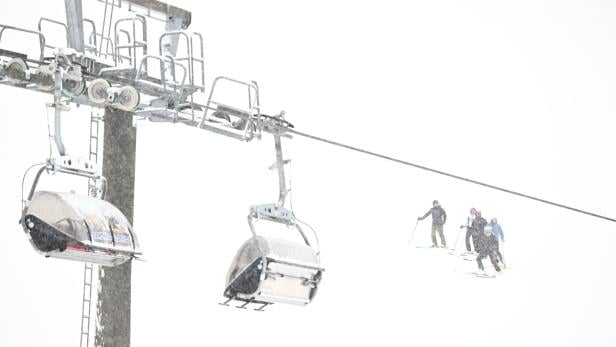 Eine Gondelbahn schwebt über Skifahrer in dichtem Schneefall.