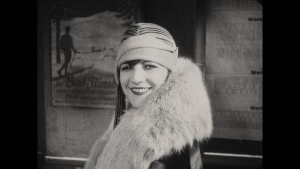Die Schauspielerin Ellen Richter, mit Pelzstola und Kopftuch, lächelt in die Kamera, Standbild aus einem Film