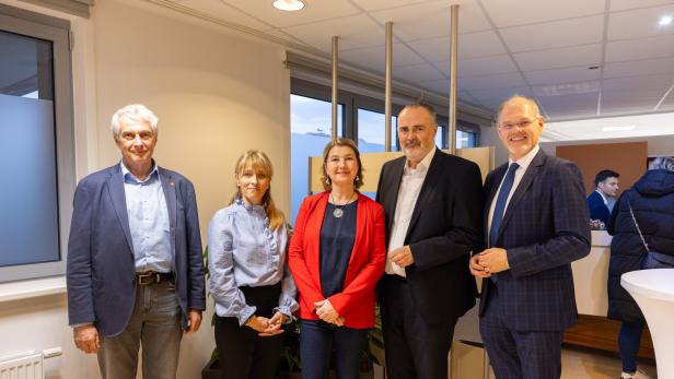 Fünf Personen stehen nebeneinander in einem modernen, hellen Raum und lächeln in die Kamera.