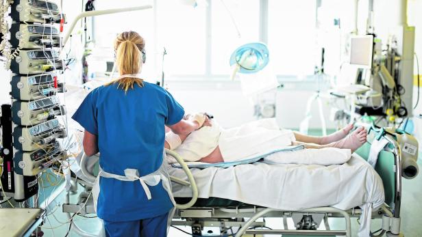 Eine Krankenpflegerin steht mit dem Rücken zur Kamera vor einem Patienten, den sie gerade behandelt.