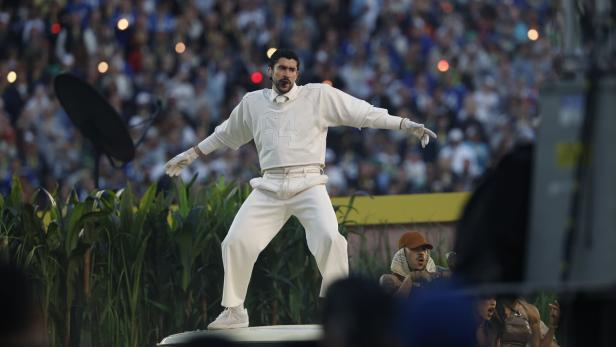 Bad Bunny performt in weißem Outfit vor einer jubelnden Menschenmenge.