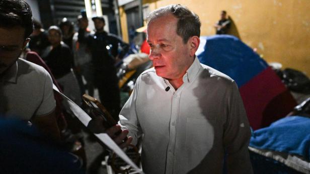 Ein Mann im weißen Hemd steht nachts vor bunten Zelten und spricht mit einer weiteren Person.