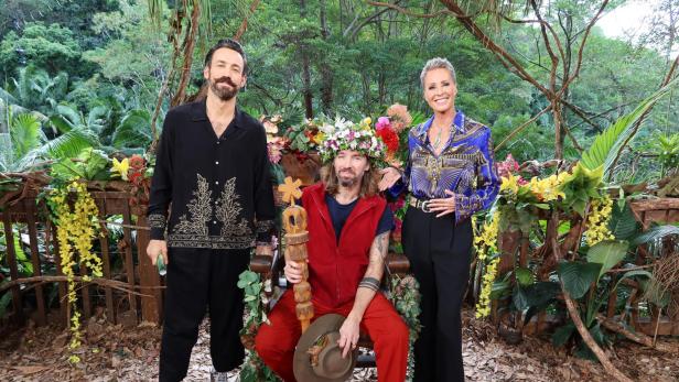 Gil Ofarim sitzt mit Dschungelkrone und Zepter zwischen den Moderatoren Sonja Zietlow und Jan Köppen im australischen Dschungelcamp.