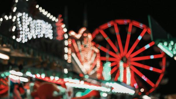 Bunte Lichter und ein Riesenrad auf einem unscharf aufgenommenen Jahrmarkt bei Nacht.
