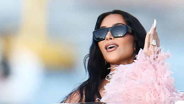 Kim Kardashian mit Sonnenbrille gestikuliert mit einem Ring am Finger.