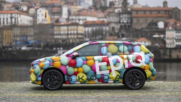 Škoda Epiq mit bunter Camouflage-Folierung vor einer historischen Stadtansicht am Flussufer.