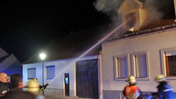 Feuerwehrleute löschen ein brennendes Haus in der Nacht.