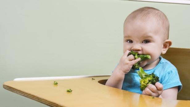 Ein Baby isst Brokkoli.