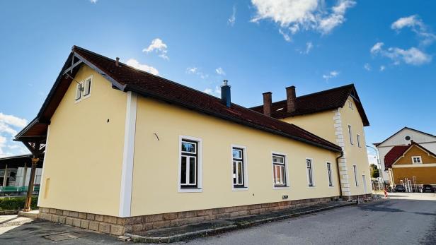 Eine Außenaufnahme vom beigen Bahnhofsgebäude vor einem blauen, fast wolkenlosen Himmel.