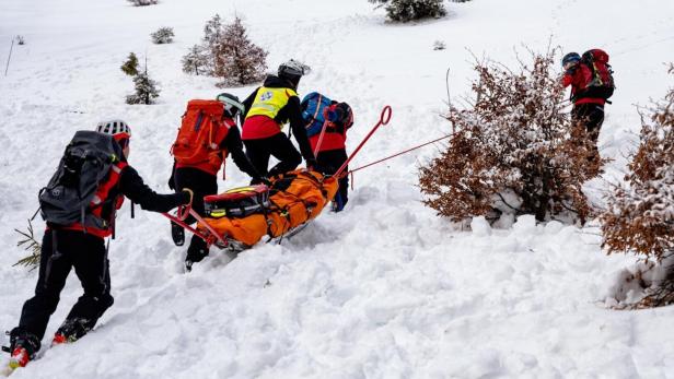 Bergretter transportieren eine Person auf einer Trage durch eine verschneite Landschaft.