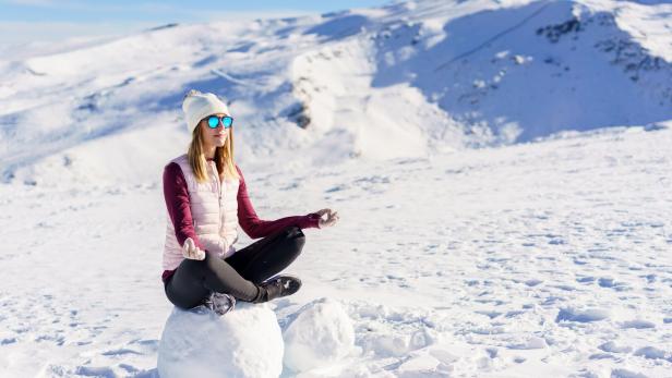 Cheerful woman sitting with lotus pose on snow