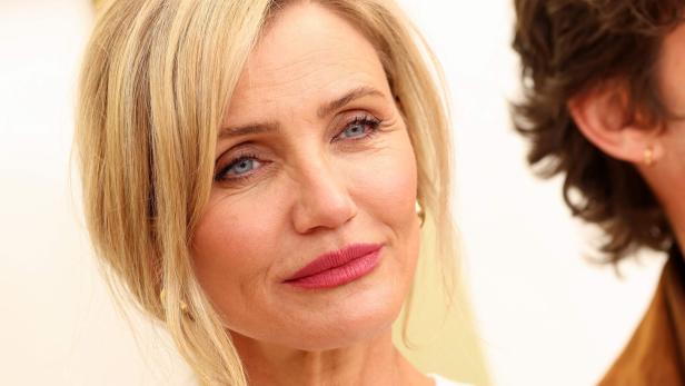 Cameron Diaz mit blonden Haaren und dezentem Make-up blickt freundlich nach vorne, im Hintergrund ist eine weitere Person teilweise sichtbar.