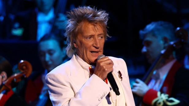 Rod Stewart singt mit einem Mikrofon in der Hand vor einem Orchester.