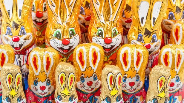 Viele goldene Schokoladenhasen mit aufgemalten Gesichtern stehen dicht nebeneinander.